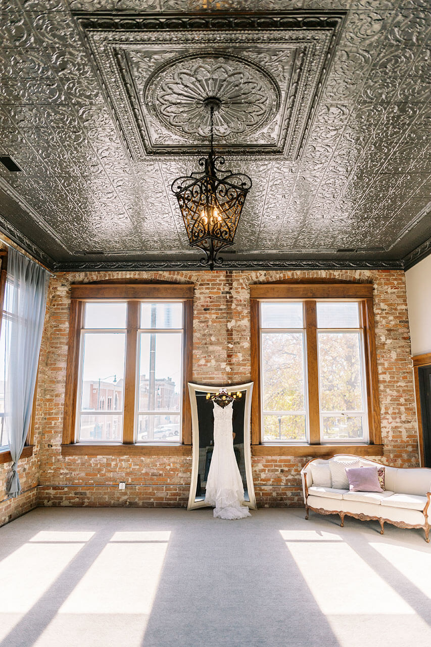 Sunlit bridal suite with a wedding dress on display under a decorative tin ceiling