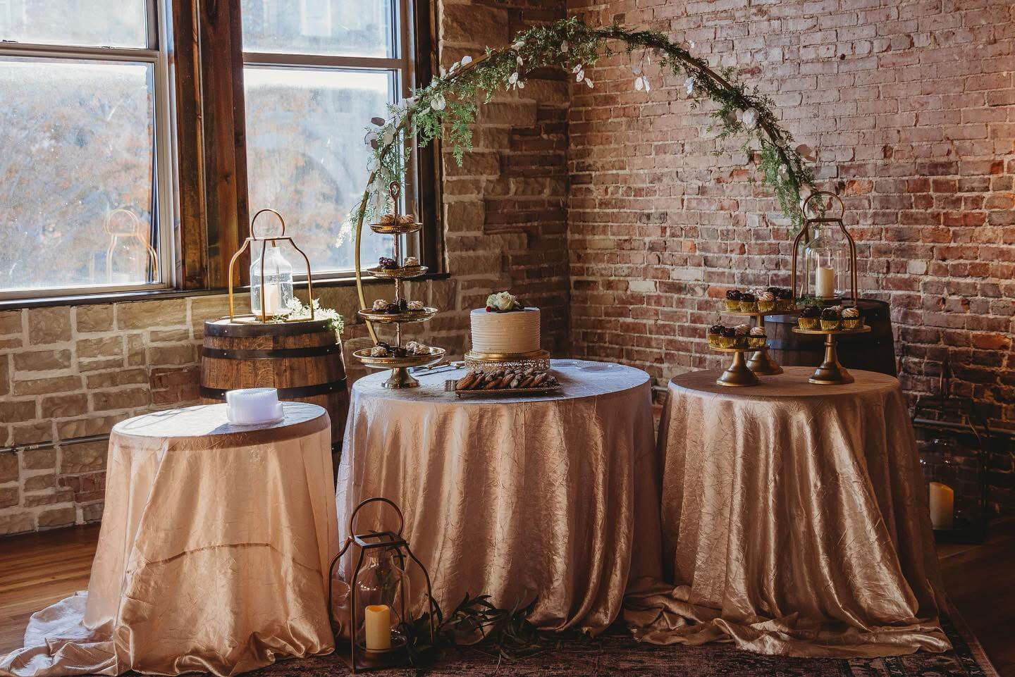 Indoor cake and dessert display on champagne linens against exposed brick